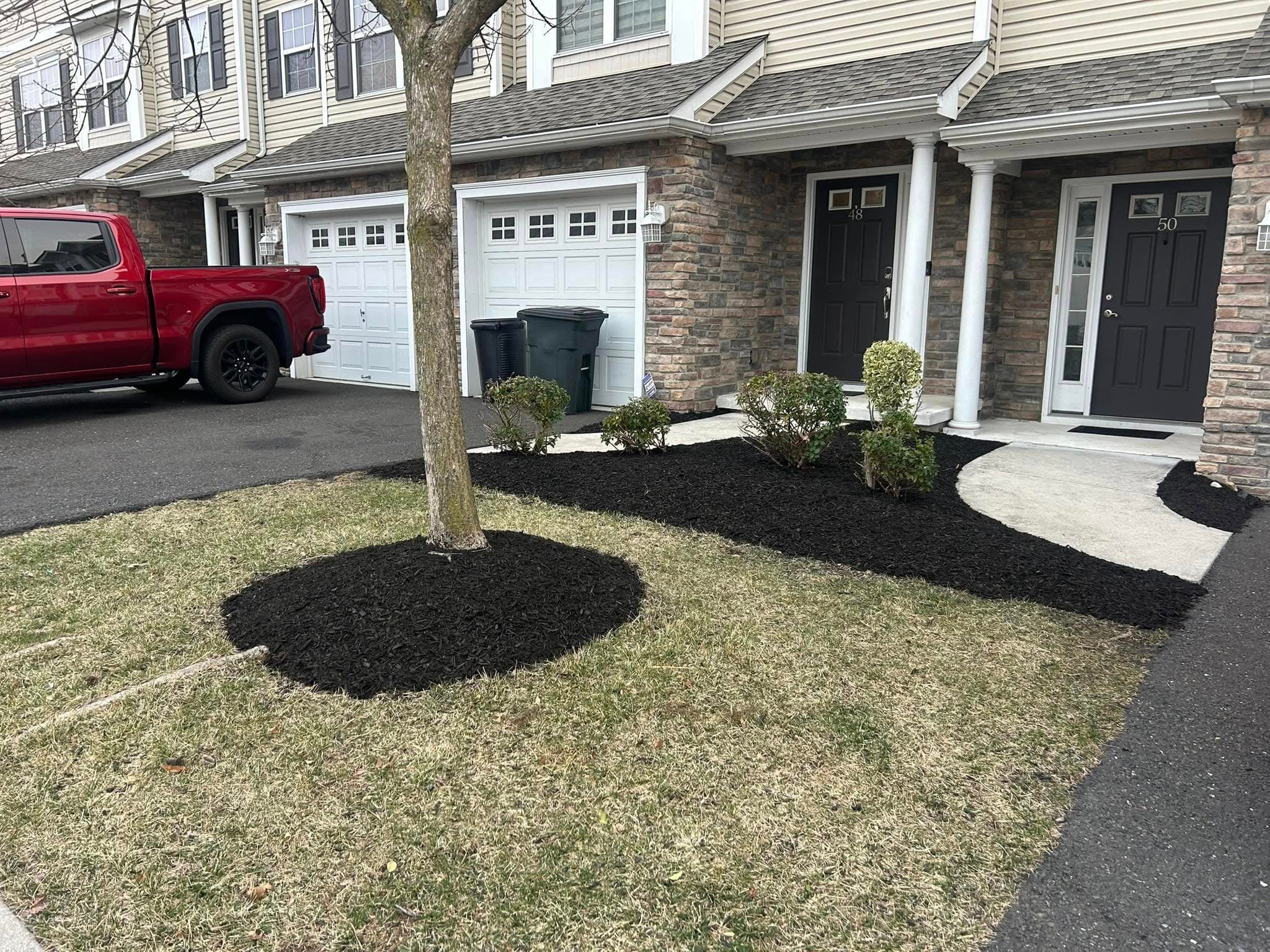 Landscaped front yard with mulch, shrubs, and a truck parked outside a townhouse.