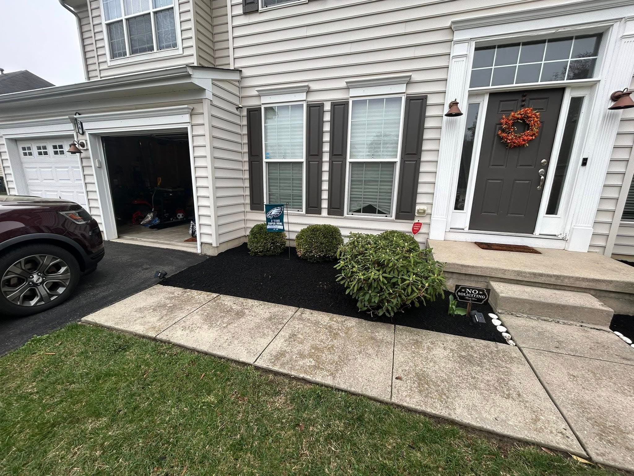 Front entryway of a house with landscaping, black mulch, and festive wreath on the door.